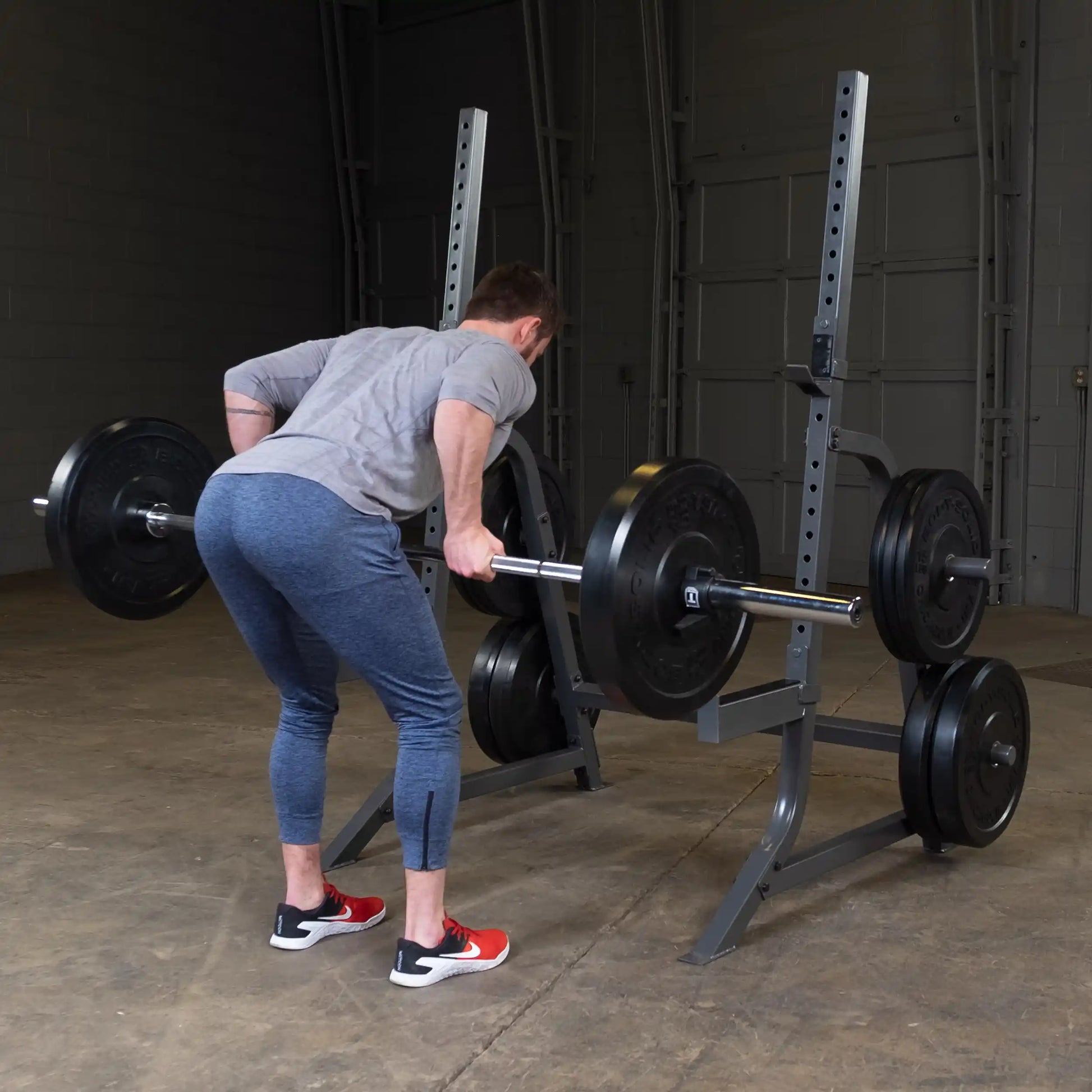 A person in athletic wear performing a deadlift with a barbell loaded with weights in a gym setting. The individual is focused on their form, with the barbell positioned near their shins as they prepare to lift.