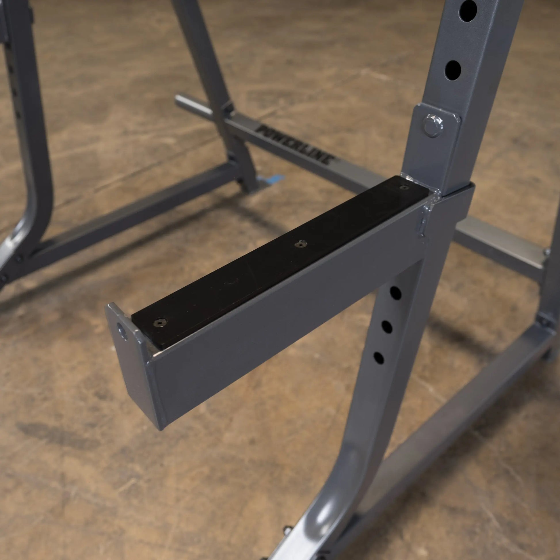 Close-up of a metal gym equipment component with a black padded surface, part of a weightlifting rack, showcasing its sturdy construction and adjustable features.