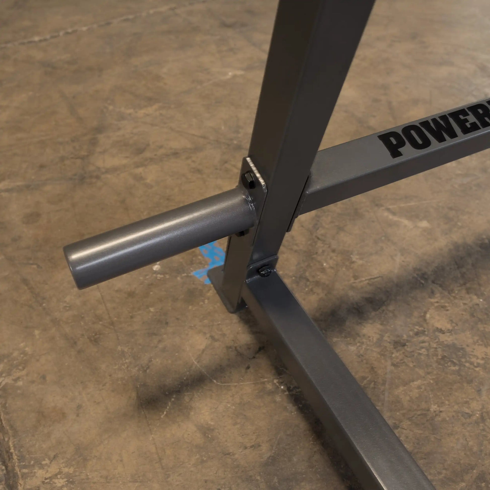 Close-up of a weightlifting equipment frame featuring a silver tube attachment and the word 'POWER' printed on the side, set against a textured concrete floor.