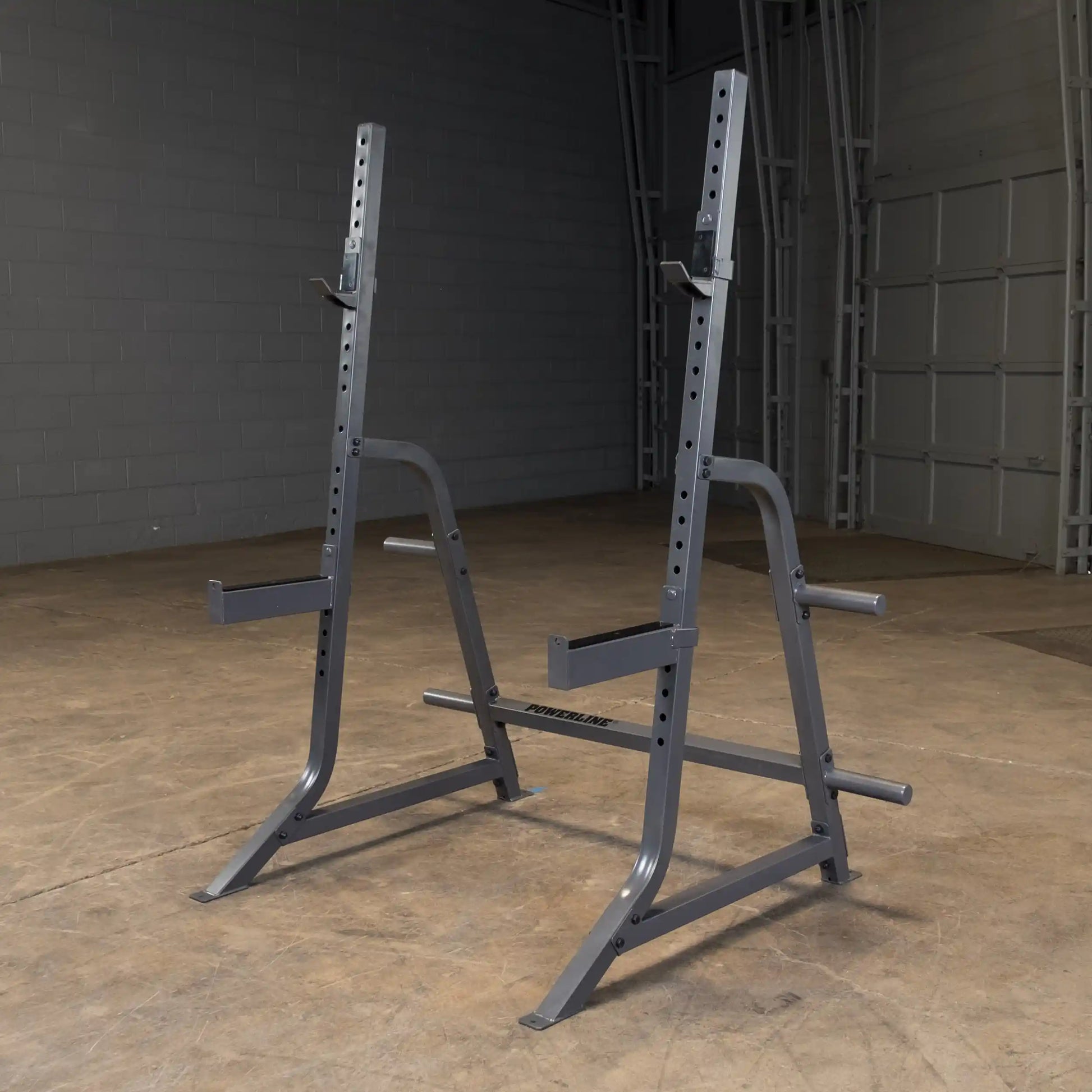 A pair of gray squat stands with adjustable heights, positioned on a gym floor with a plain background.