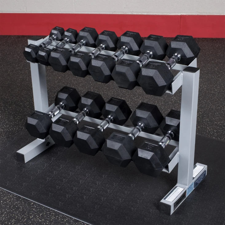 A set of black hexagonal dumbbells arranged on a metal rack in a gym, with a rubber floor surface and a red wall in the background.