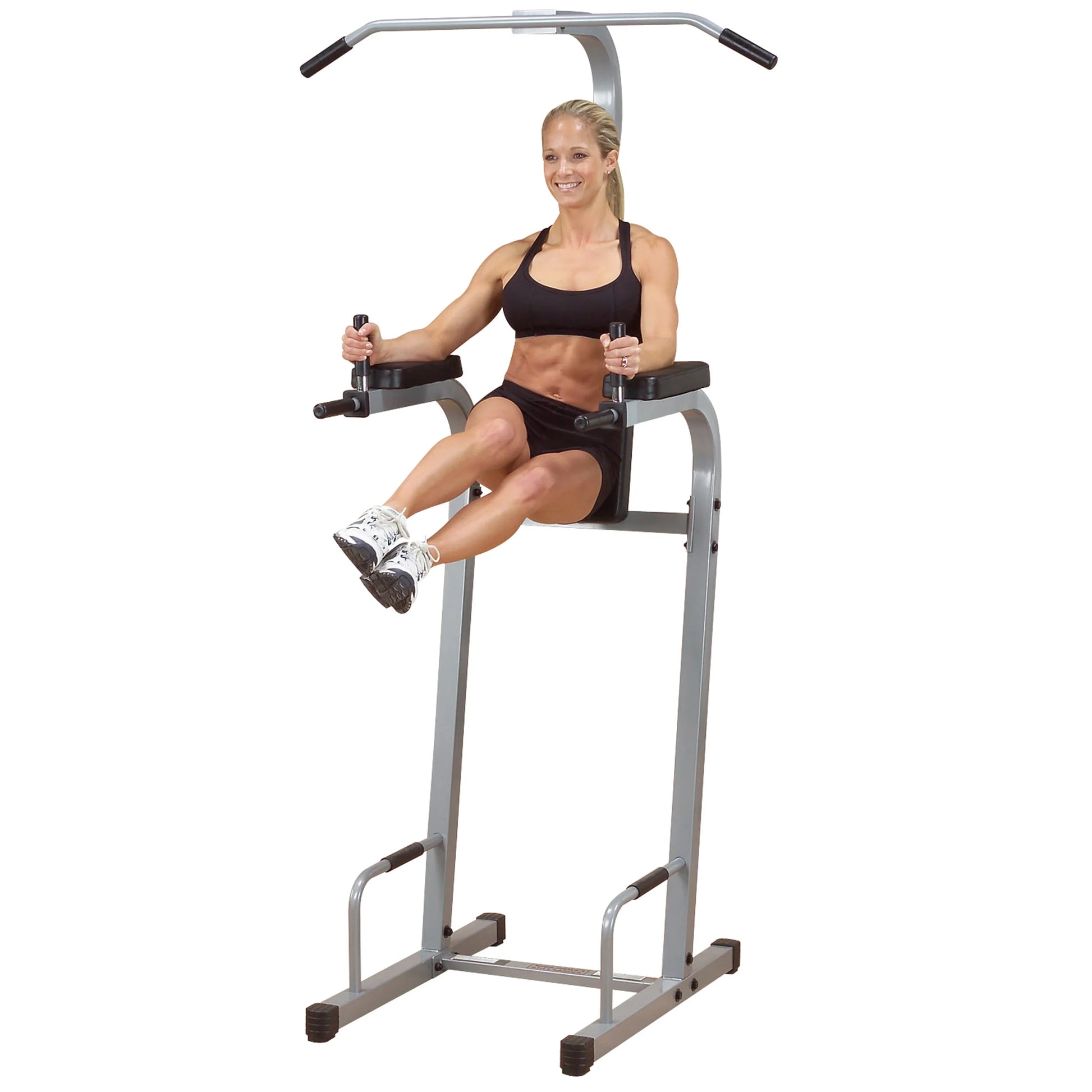 A fit woman in a black sports bra and shorts performing an exercise on a vertical knee raise machine, demonstrating strength and fitness.