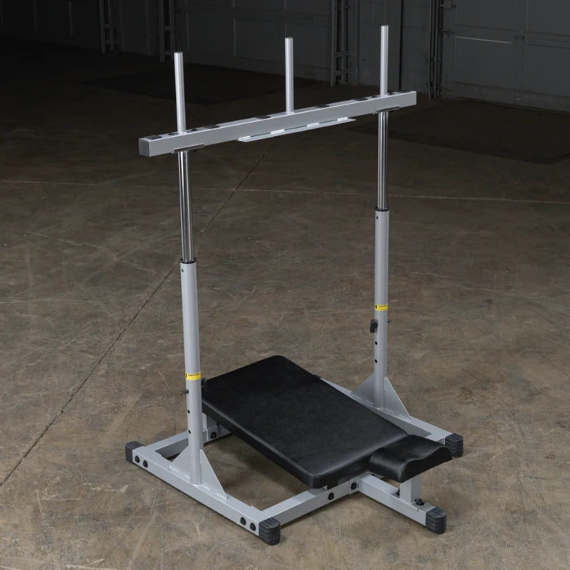 A gray weightlifting bench with a barbell rack, set up in a gym environment on a concrete floor.
