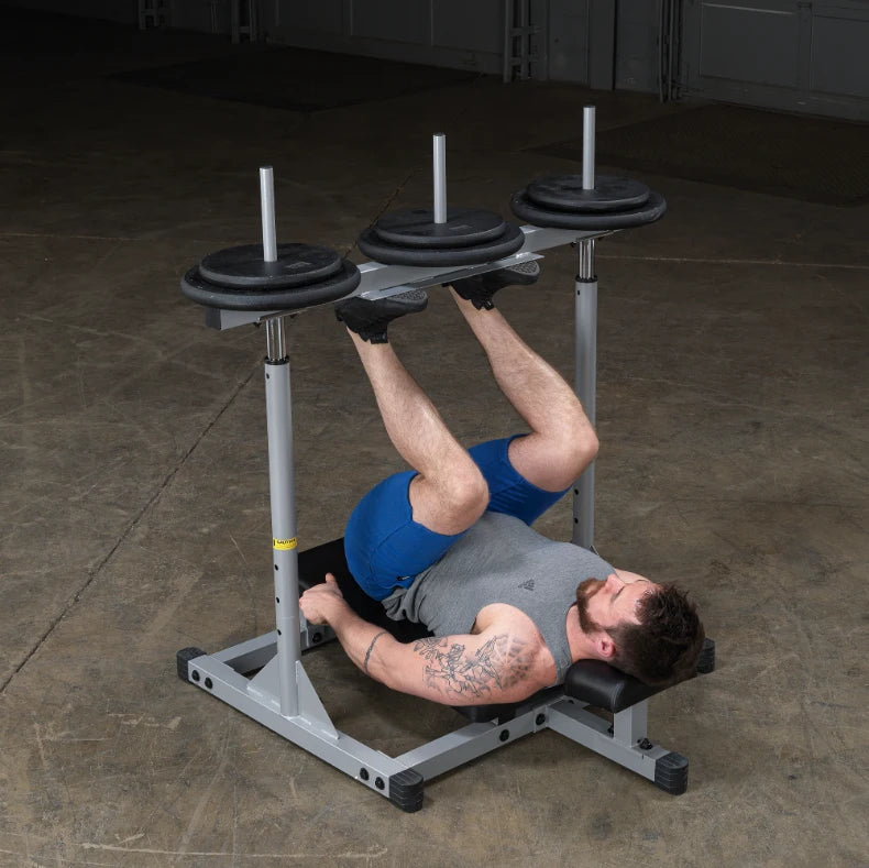 A man performing a leg exercise on a weight bench with three weight plates positioned above him in a gym setting.