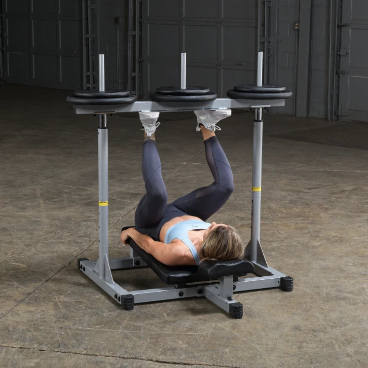 A woman performing an exercise on a weight bench with weights on either side, lying on her back with her legs raised, in a gym setting.