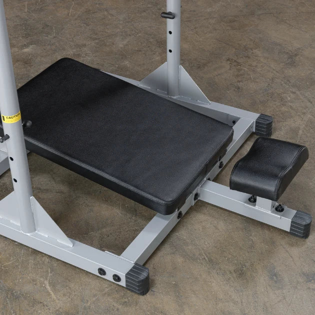 A close-up view of a weight bench with a black padded seat and a small footrest, set on a gray metal frame, placed on a concrete floor.