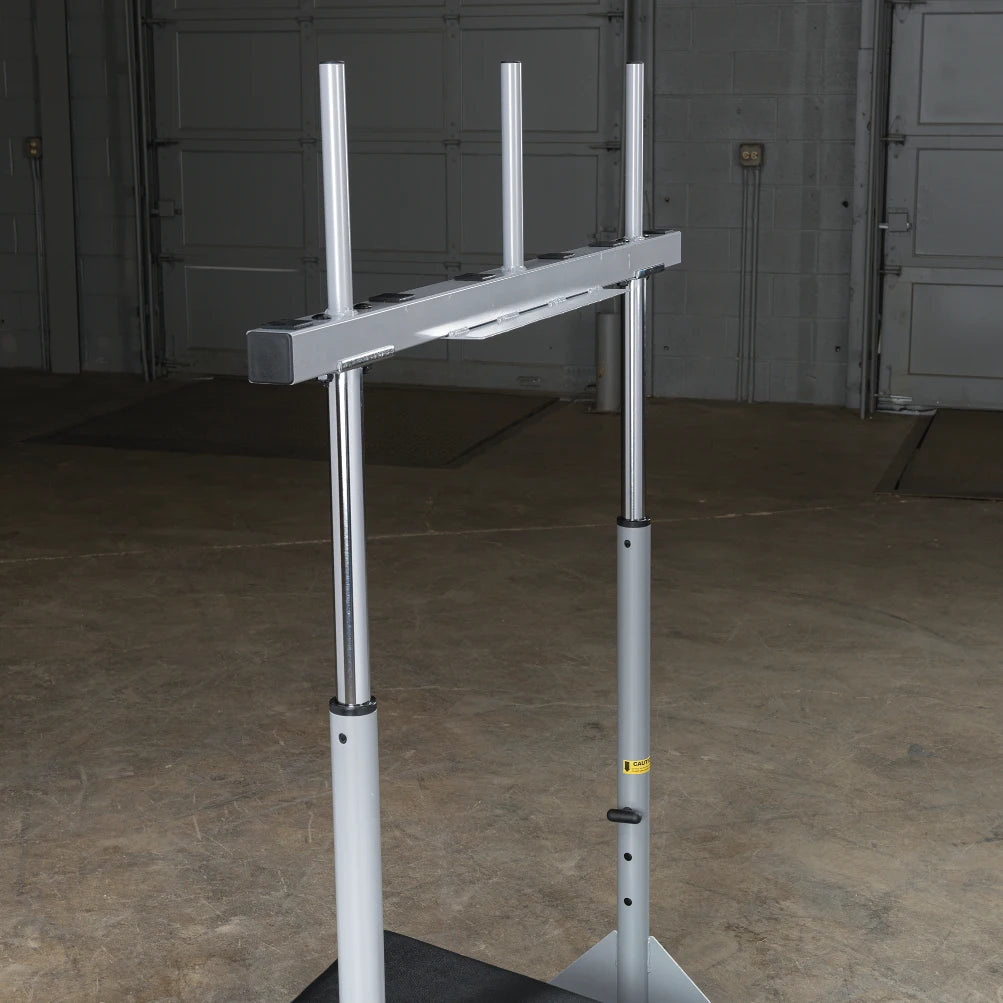 A vertical gym equipment structure with a horizontal bar at the top, set against a concrete floor and garage-style background.