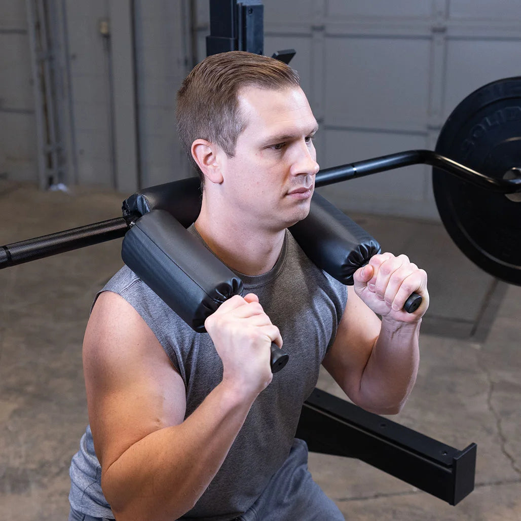 Man using black safety squat bar for weightlifting in gym.