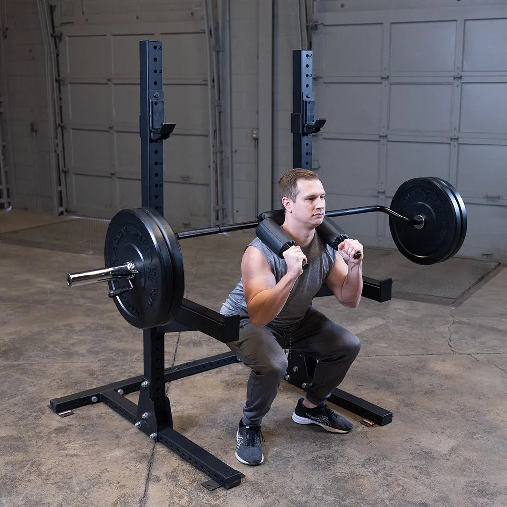 Man squatting with black safety squat bar on gym rack.