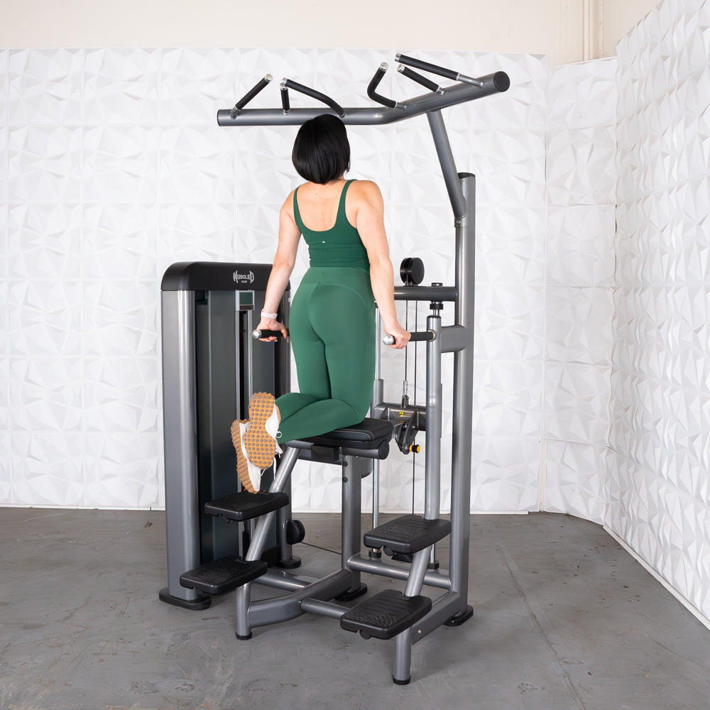 Woman exercising on a BodyKore assisted pull-up machine in green workout attire.