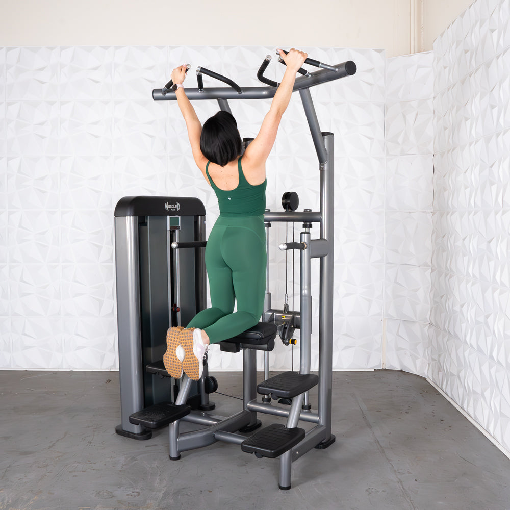 Woman in green activewear using a pull-up assist machine in a gym.