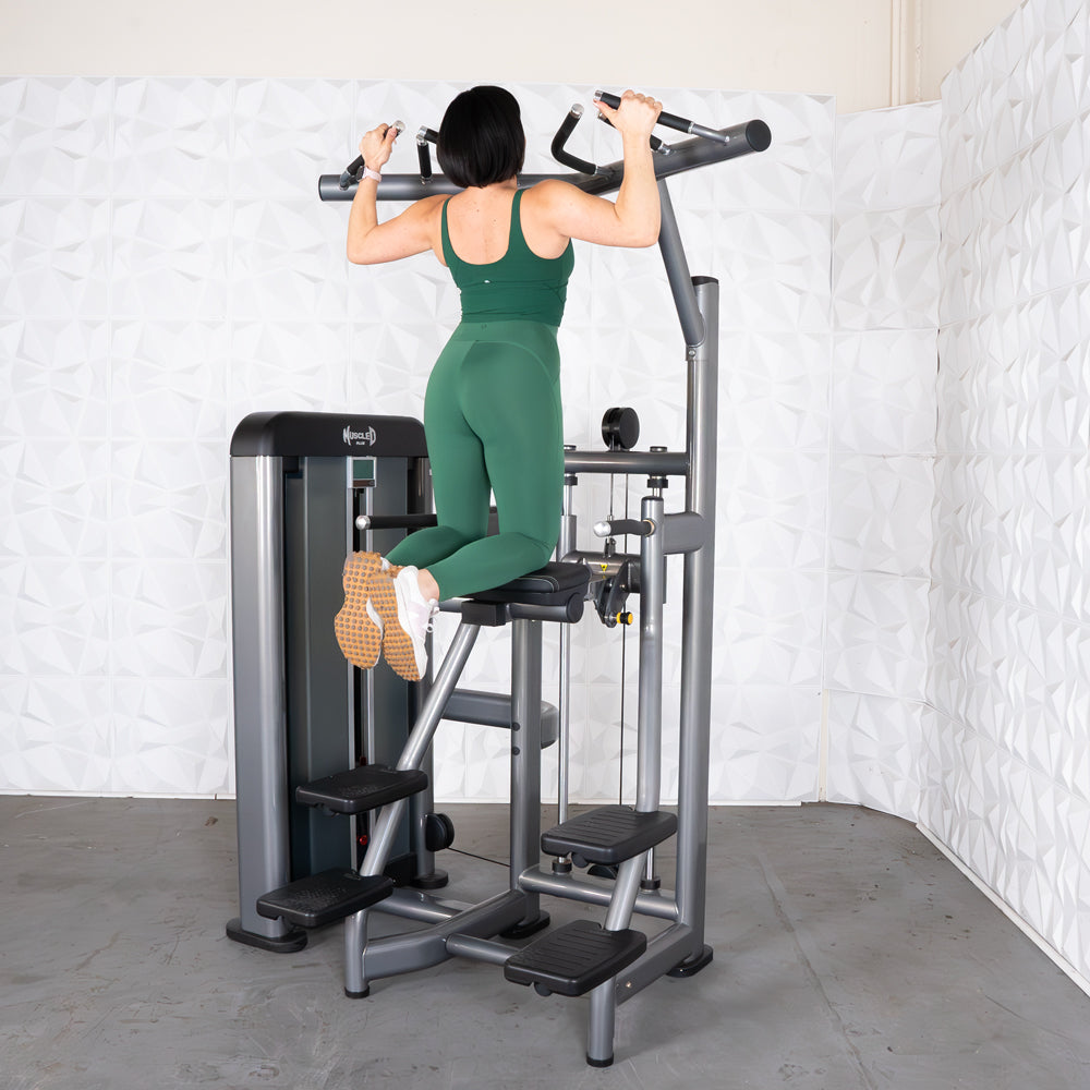 Woman in green workout attire using a pull-up assist machine in a gym setting.