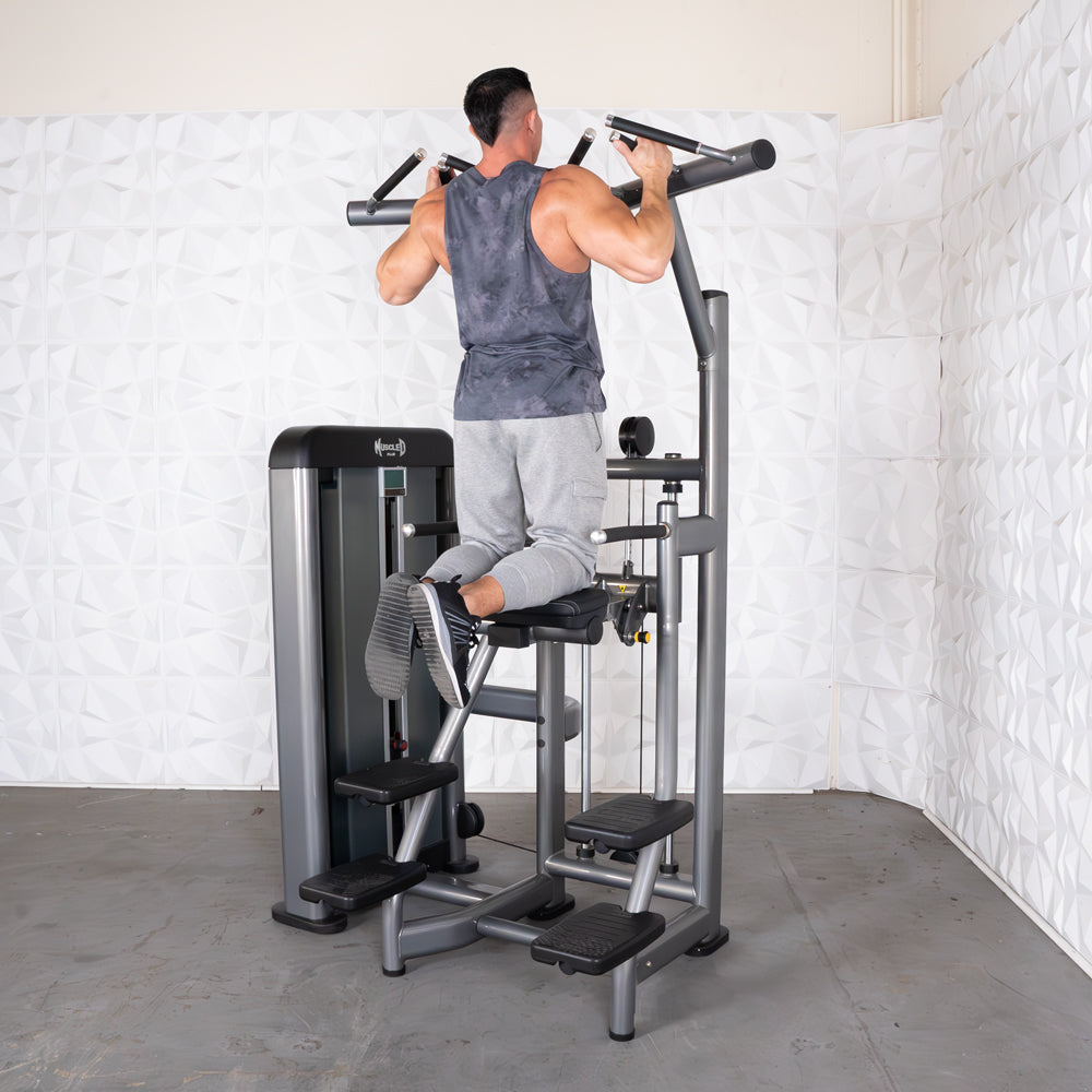 Man using Muscle D Fitness assisted pull-up machine with padded knee support.