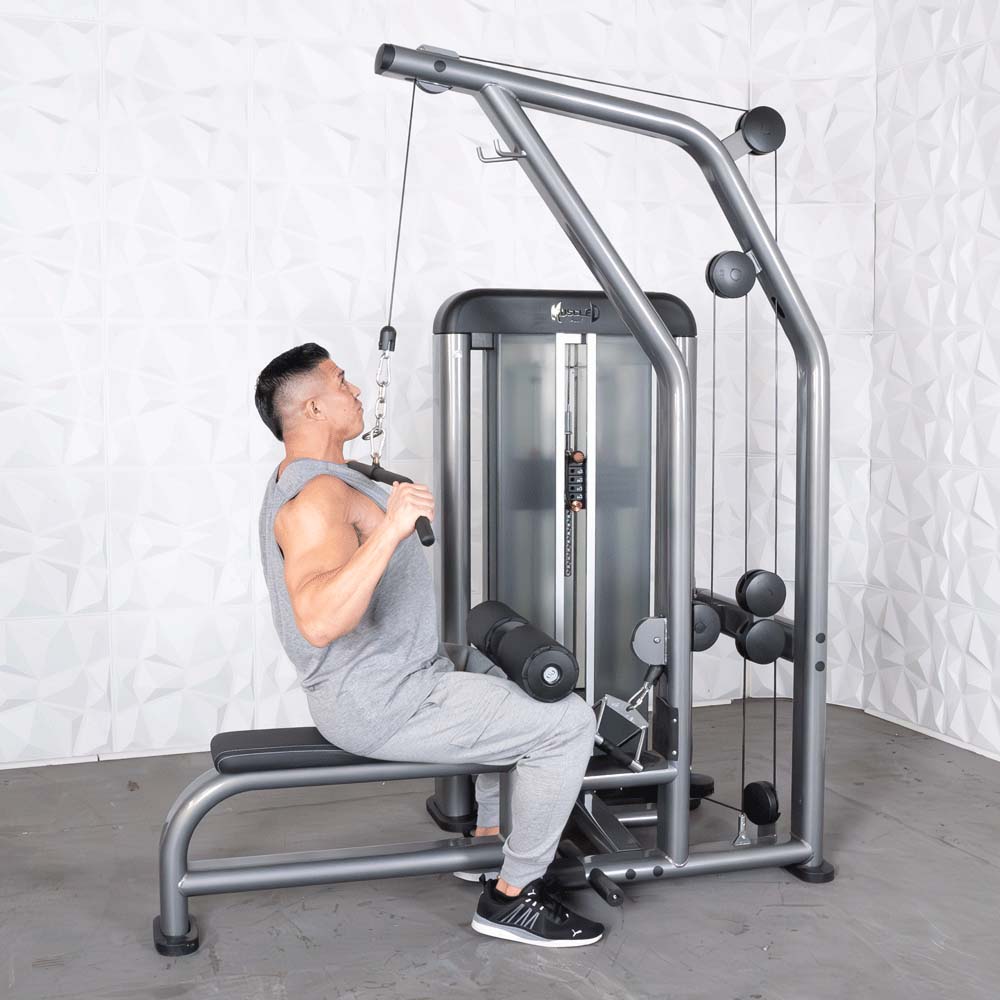 Man using a silver cable machine for lat pulldowns in a gym.
