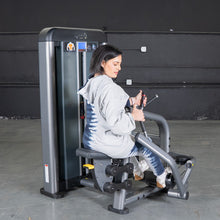 Woman using a strength training machine in a gym, featuring a sleek gray design for effective workouts.