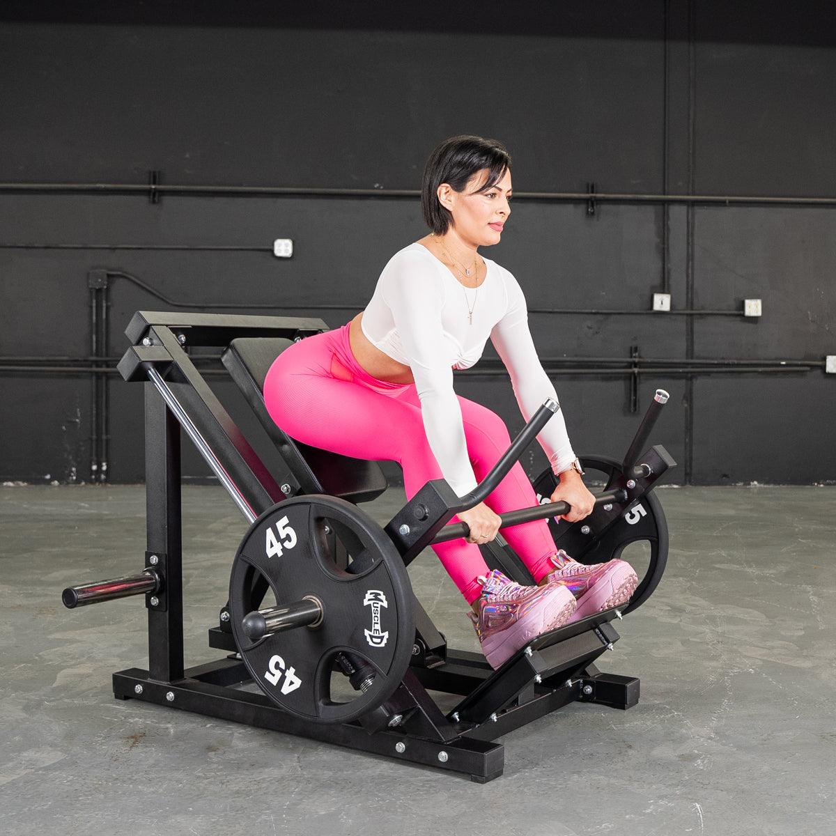 Woman using a black seated row machine in bright pink leggings at the gym.