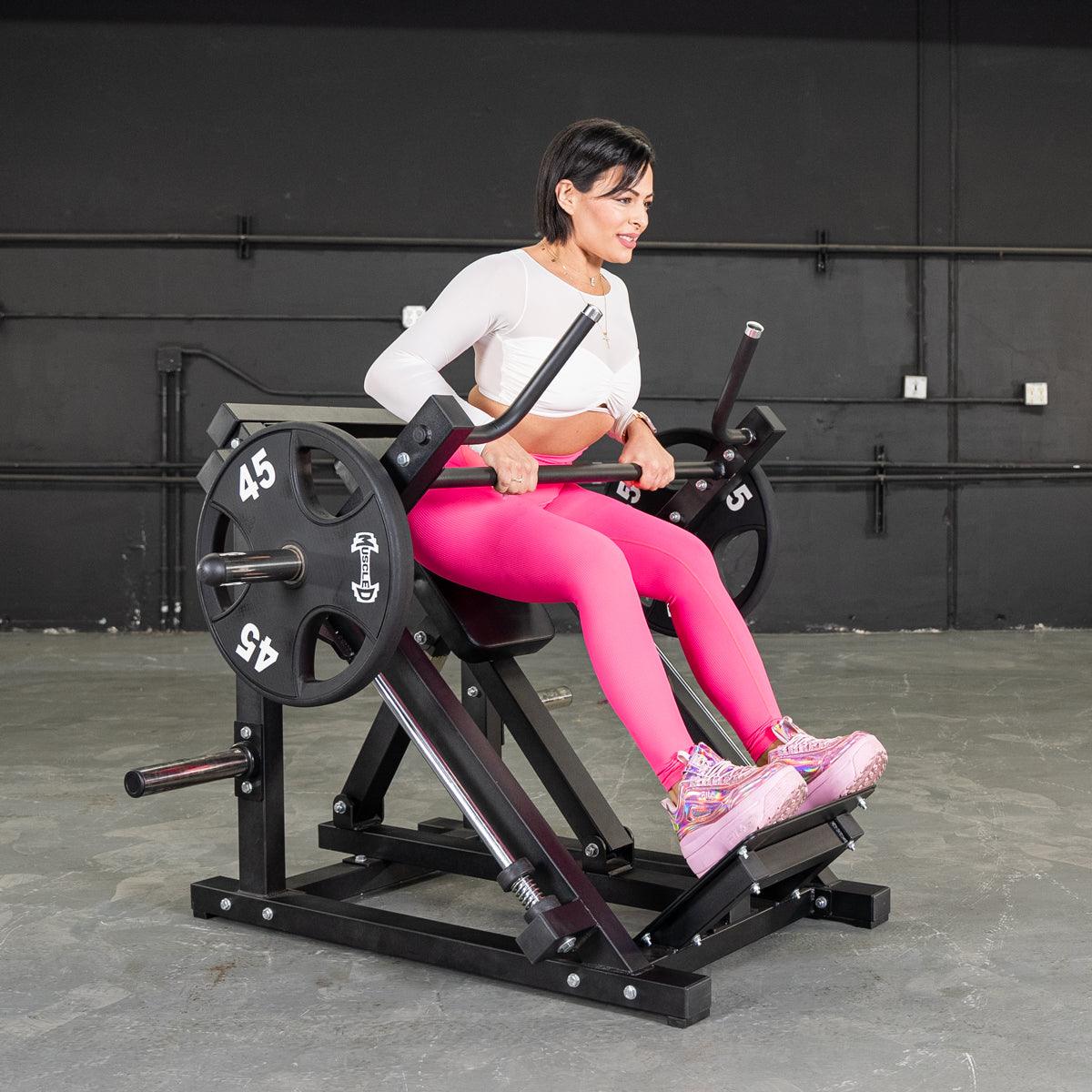 Woman using seated calf raise machine in pink leggings for strength training.