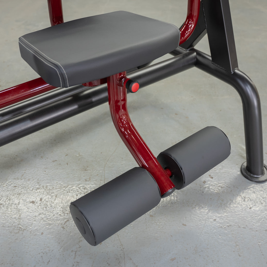 Red and black leg extension machine with padded seat for gym workouts.