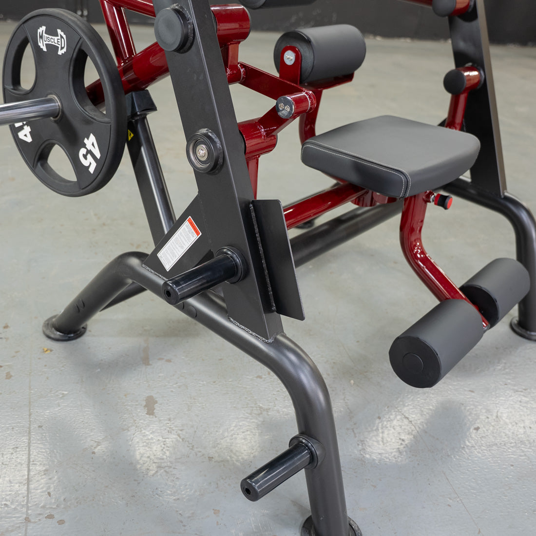 MuscleD leg extension machine with red frame and padded black seat.