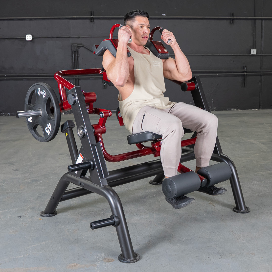 Man using a red and black squat machine for strength training in a gym.