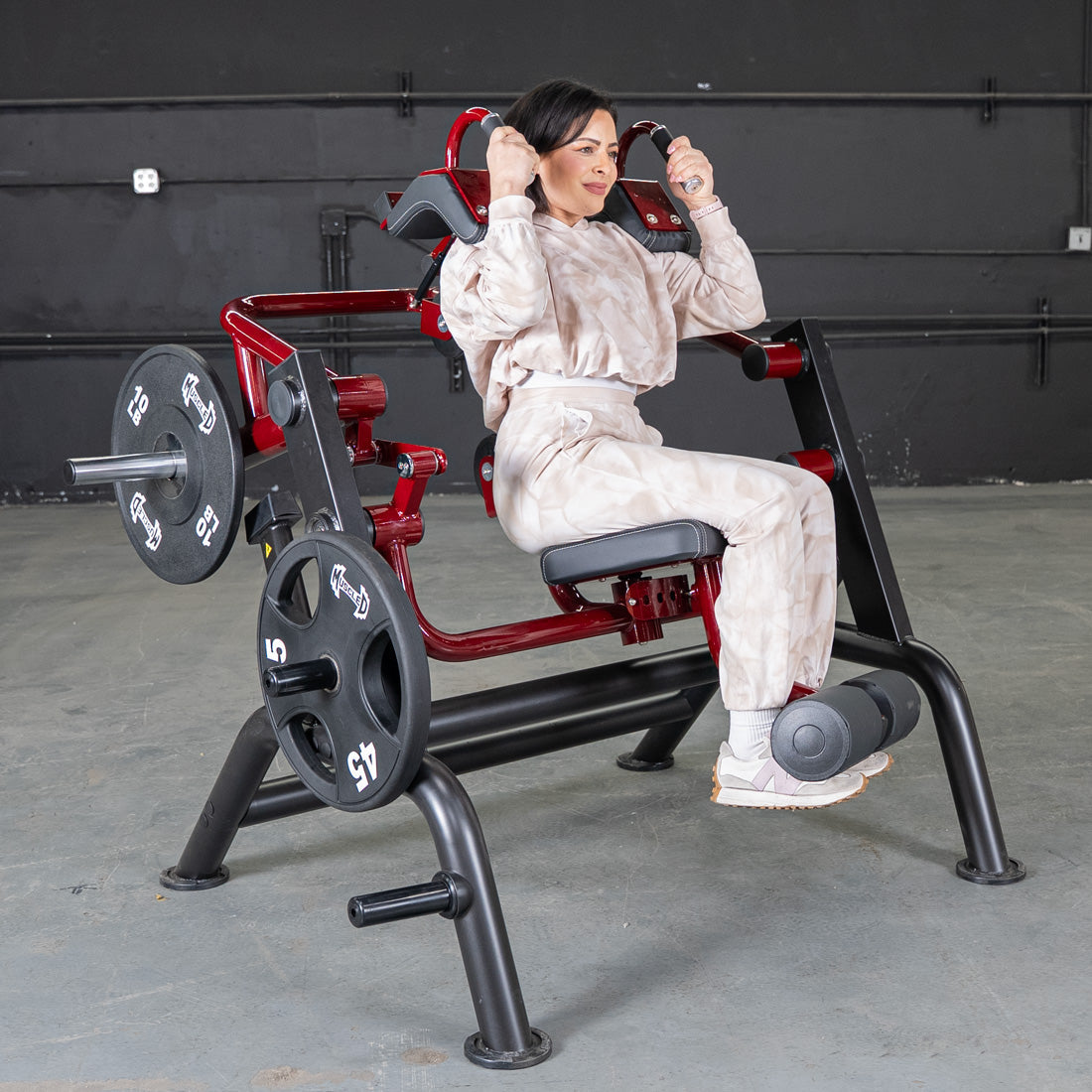 Woman using red and black plate-loaded seated crunch machine in gym.