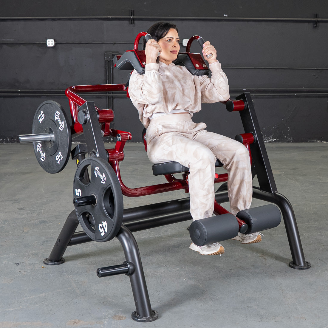 Woman using a red and black plate-loaded exercise machine in a gym.