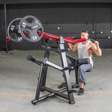 Man using red leverage shoulder press machine in gym for strength training.
