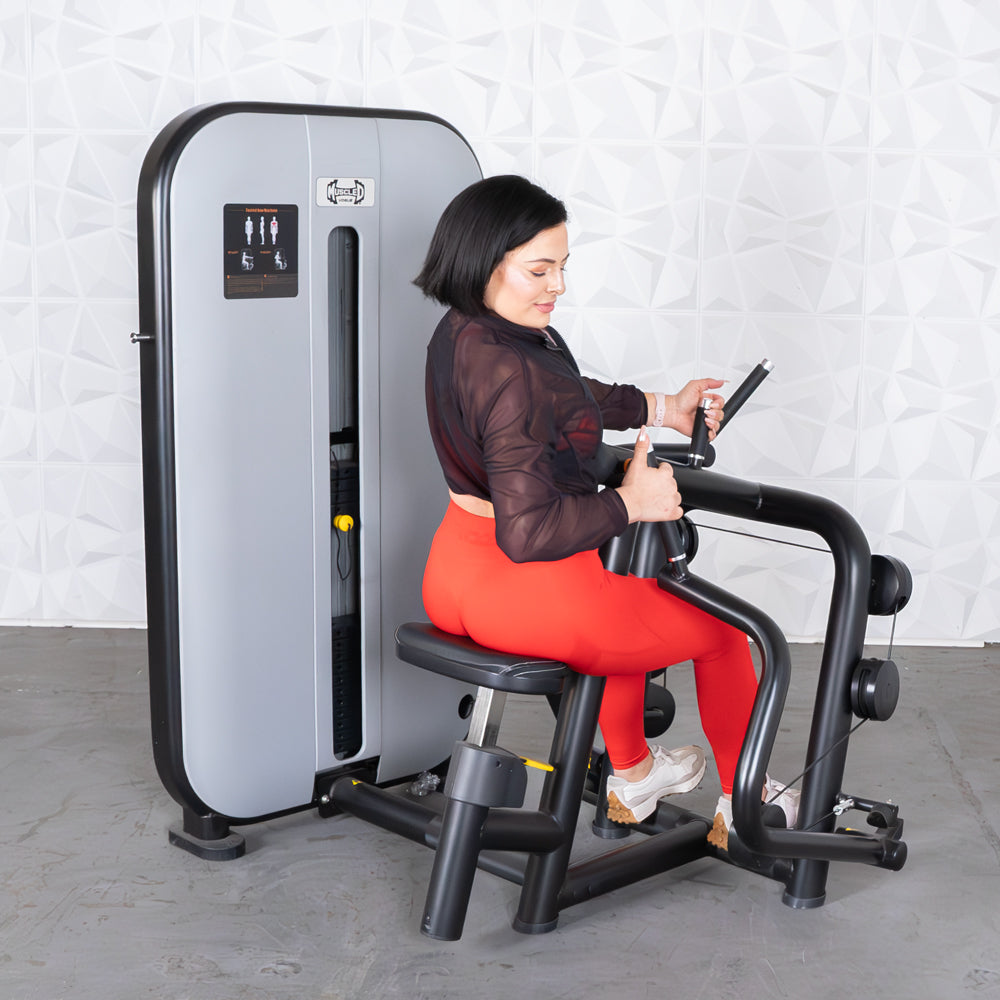 Woman using a BodyKore back extension machine in a gym, wearing bright red leggings.