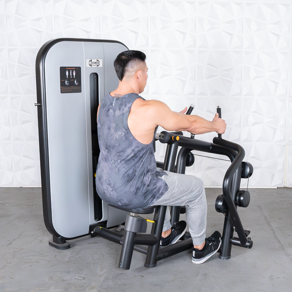 Man using seated row machine in gym, wearing grey tank top and joggers.