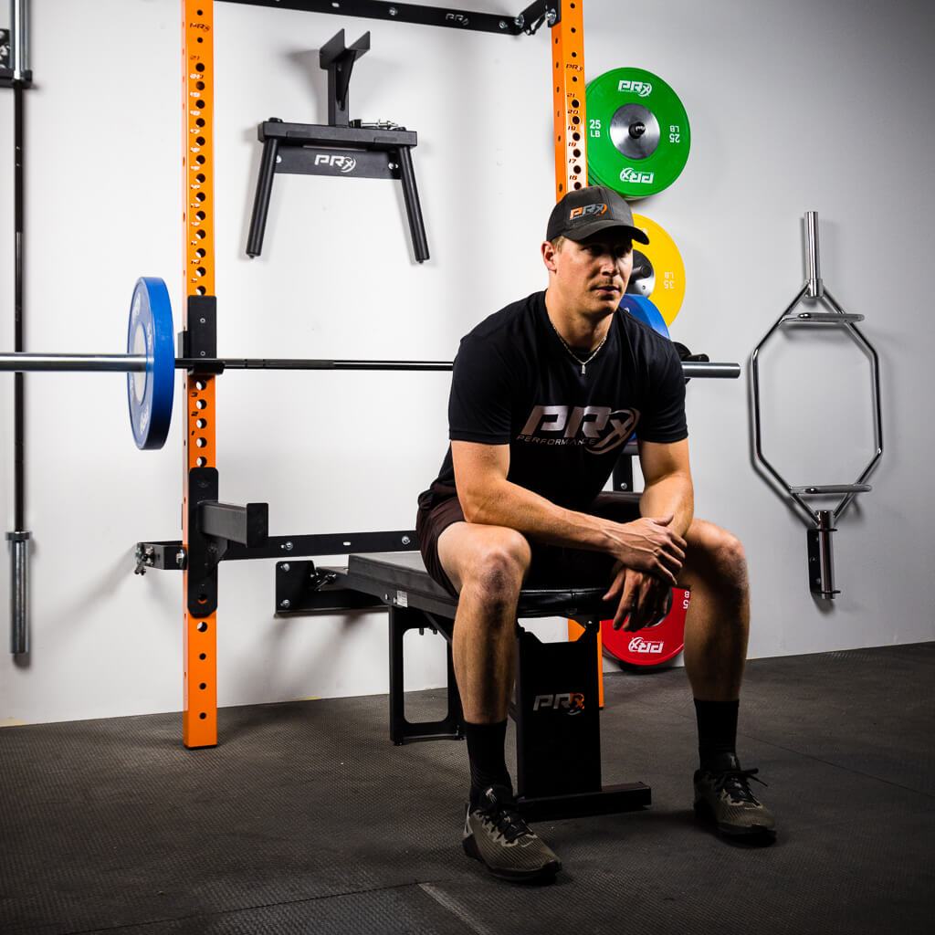Man sitting on a PRx flat-folding bench in a gym with barbells and plates.