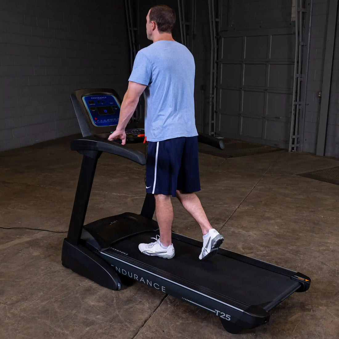 Man walking on a Body-Solid Endurance T25 treadmill with one hand on the handrail