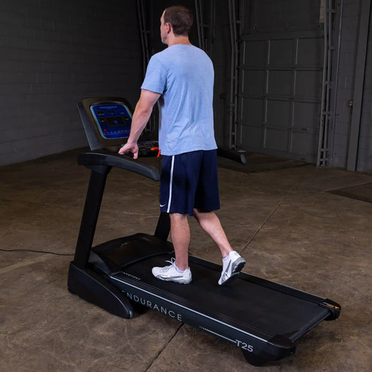 Man walking on a Body-Solid Endurance T25 treadmill with one hand on the handrail