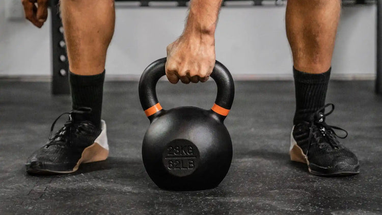 Man holding black and orange cast icon kettlebell in a gym setting