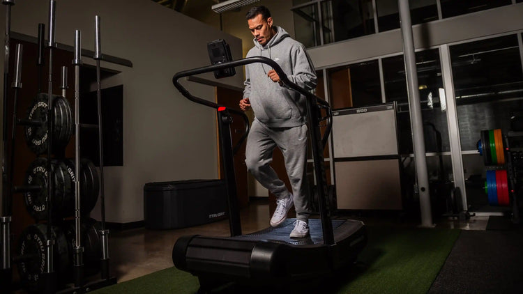 Man in grey hoodie running on a curved treadmill in gym setting