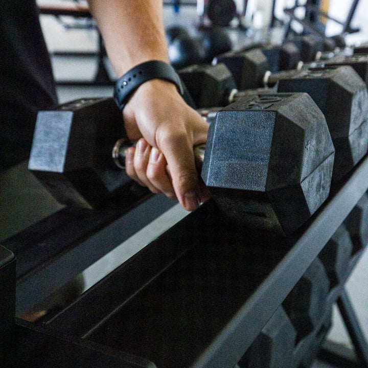 Close-up of a hand gripping a hexagonal dumbbell on a rack.