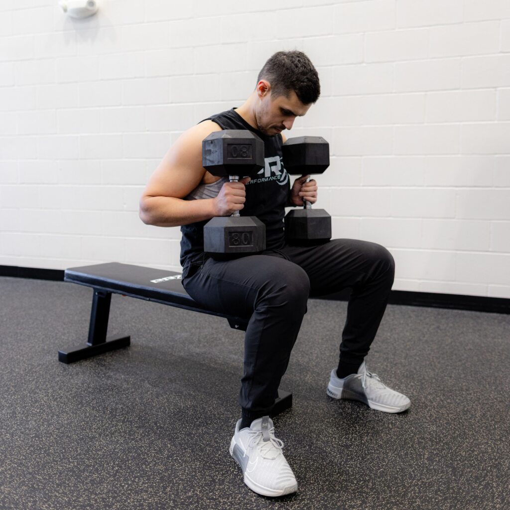 Man in gym bench doing dumbbell curls with two heavy dumbbells.