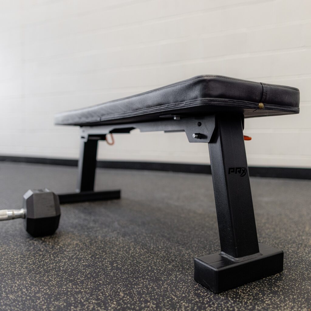 Black adjustable workout bench in a gym, with a dumbbell on the floor.