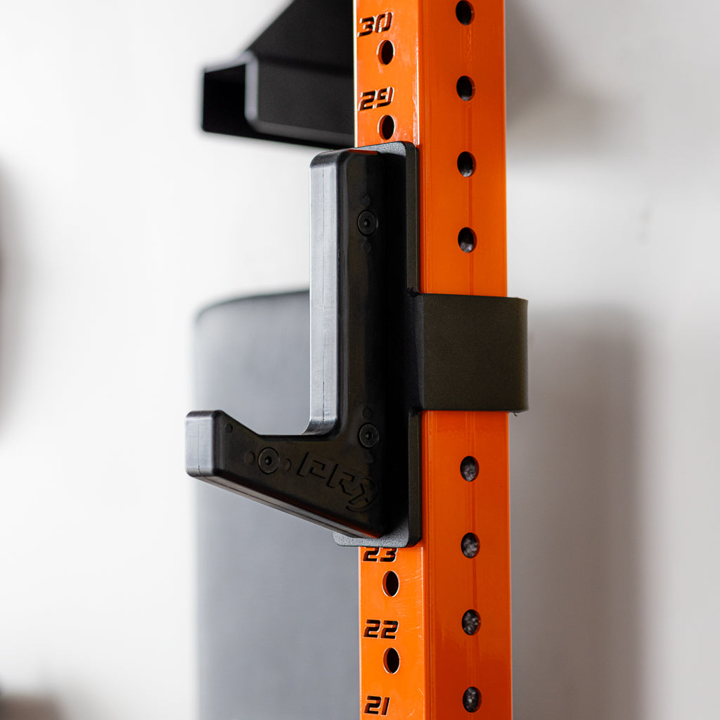Close-up of orange gym squat rack with black J-hook attachment.