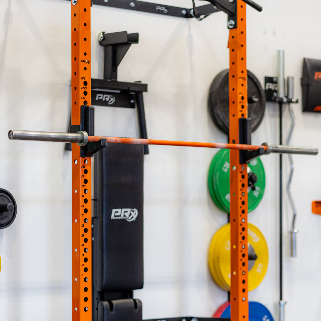Orange squat rack with a barbell across; weight plates visible in the background.