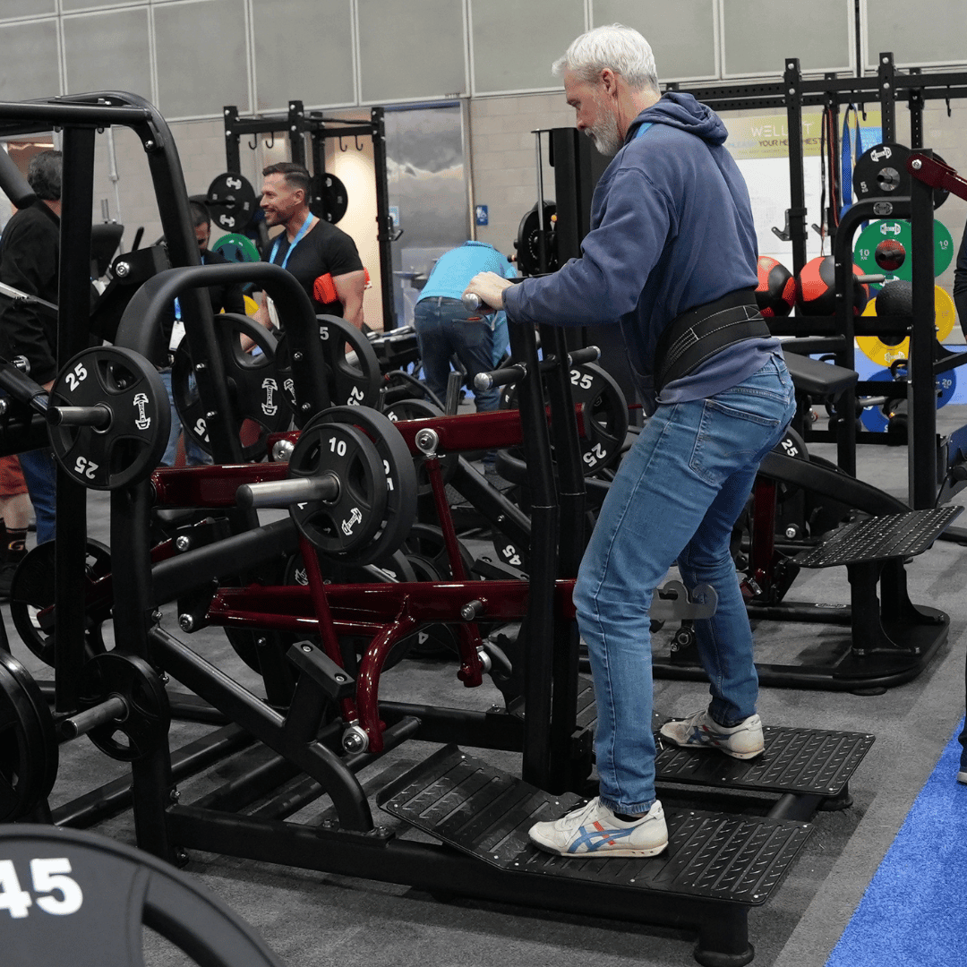 Older man in blue hoodie using leg extension machine at gym.
