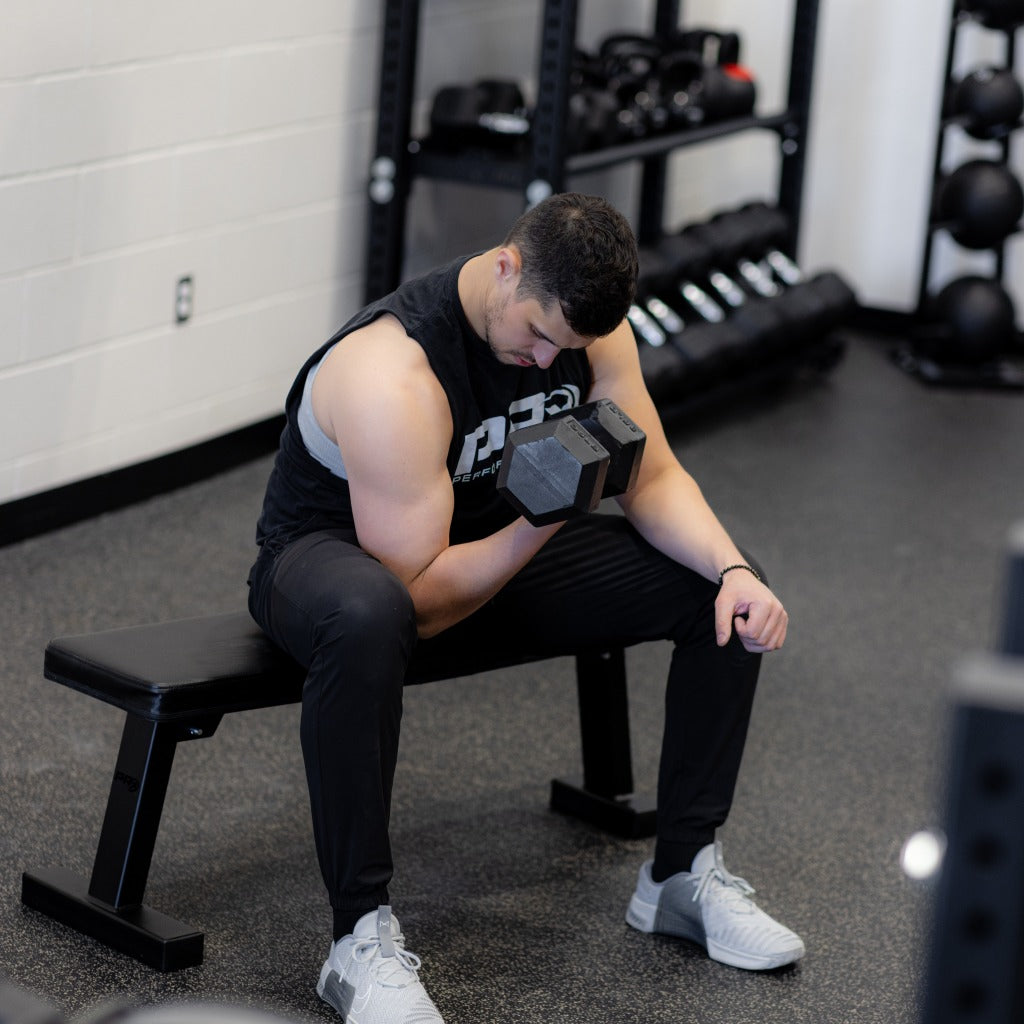 Athlete seated on bench in gym, performing a dumbbell curl.