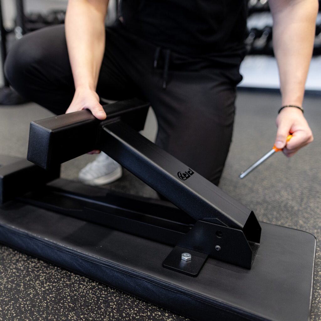Person assembling a black gym leg extension machine with a screwdriver.