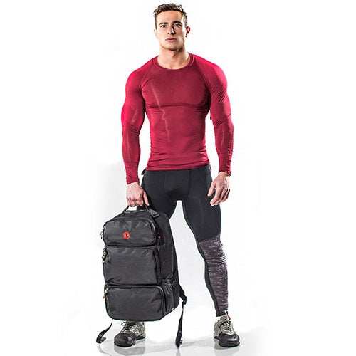 Muscular man in a red shirt holds a black backpack with multiple compartments.