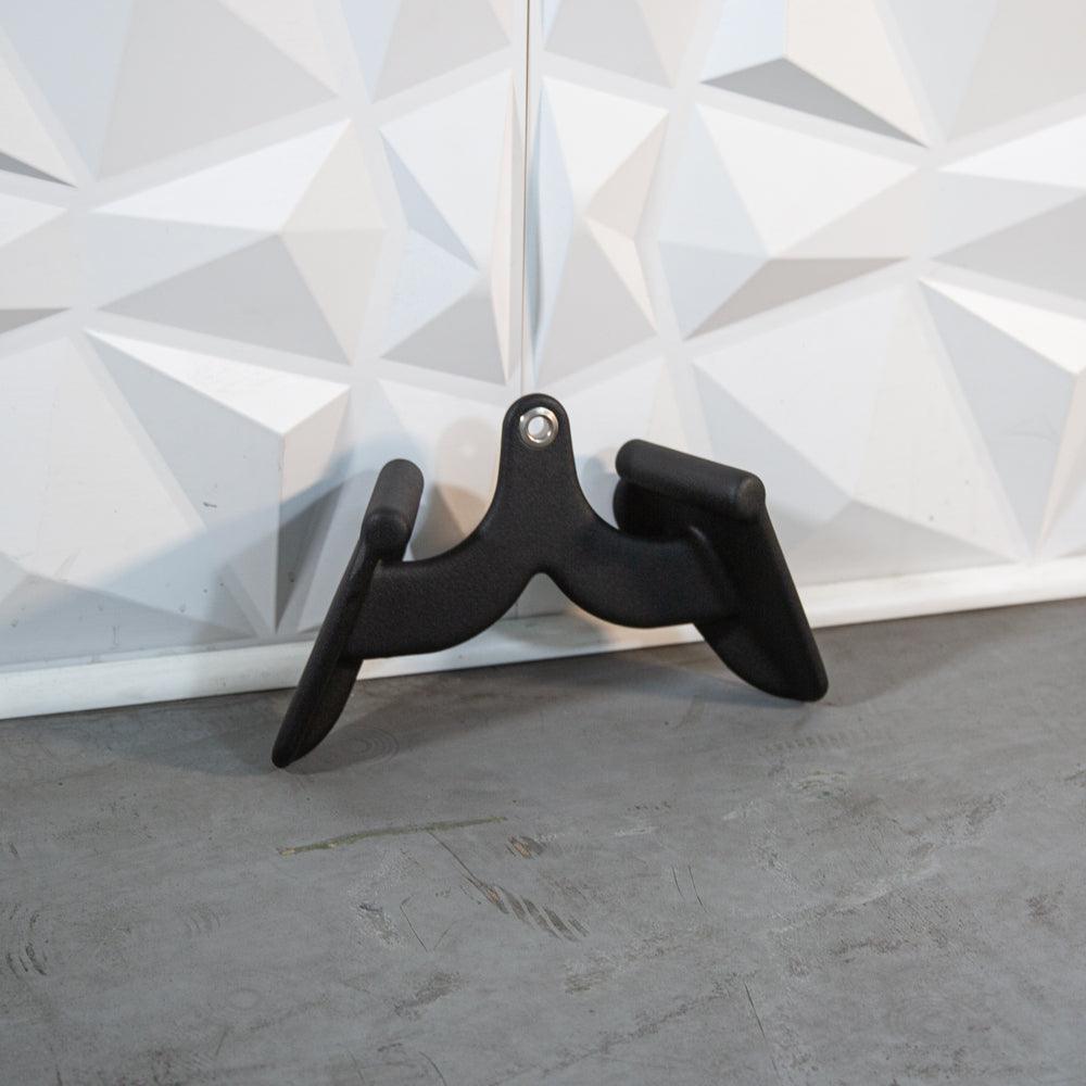 Black ergonomic handle accessory with two curved arms on a geometric white backdrop.