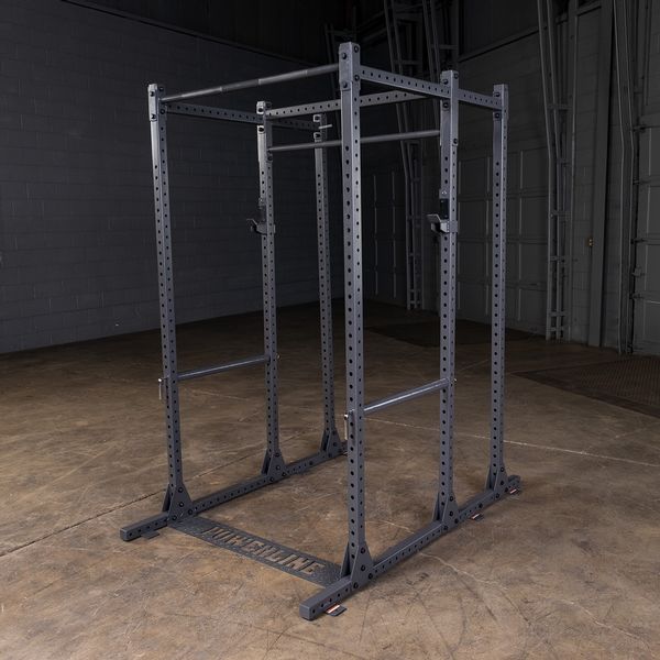 A black power rack with multiple adjustable bars, positioned in a spacious gym environment with a concrete floor and gray walls.