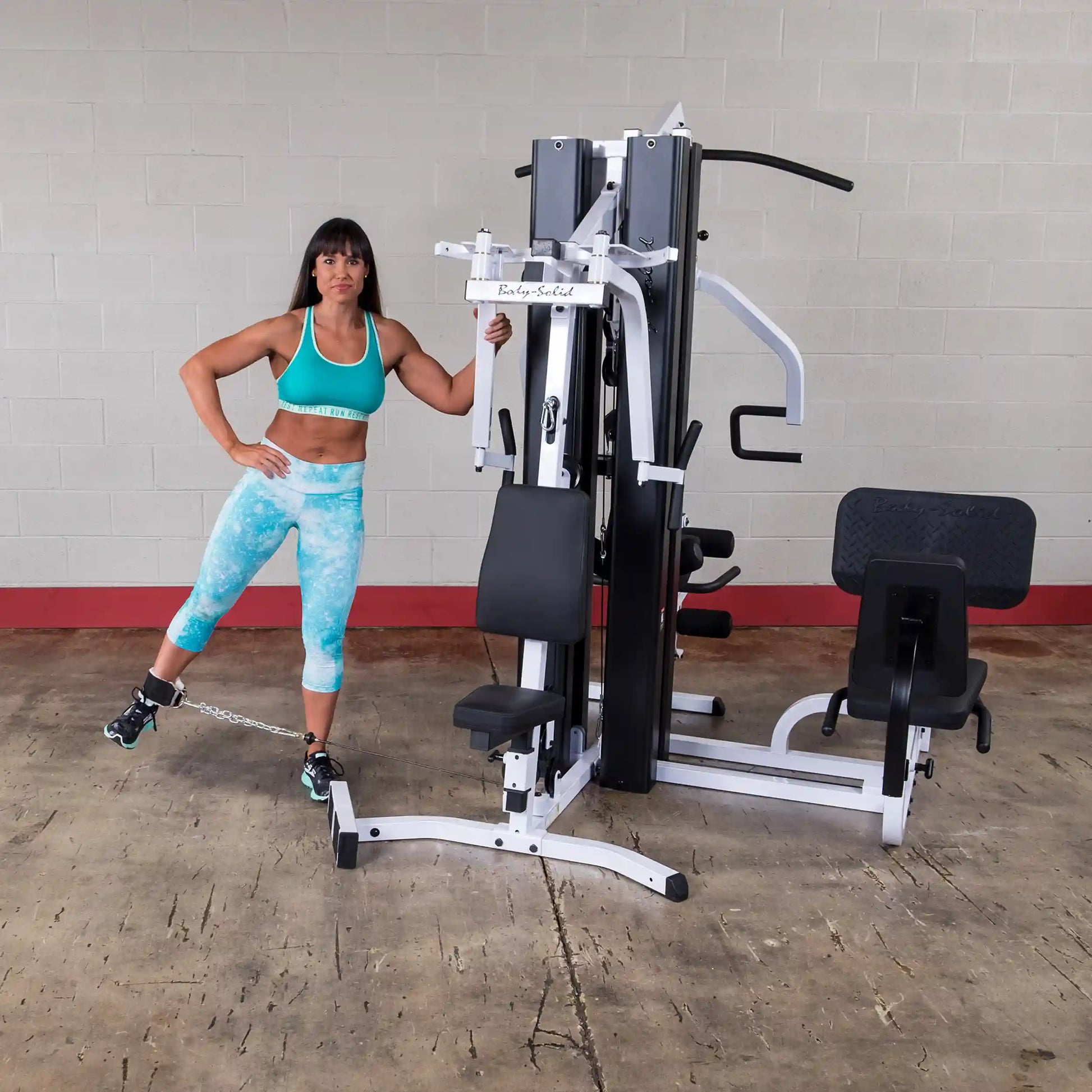Body-Solid gym machine with a woman in teal workout gear demonstrating leg exercise.