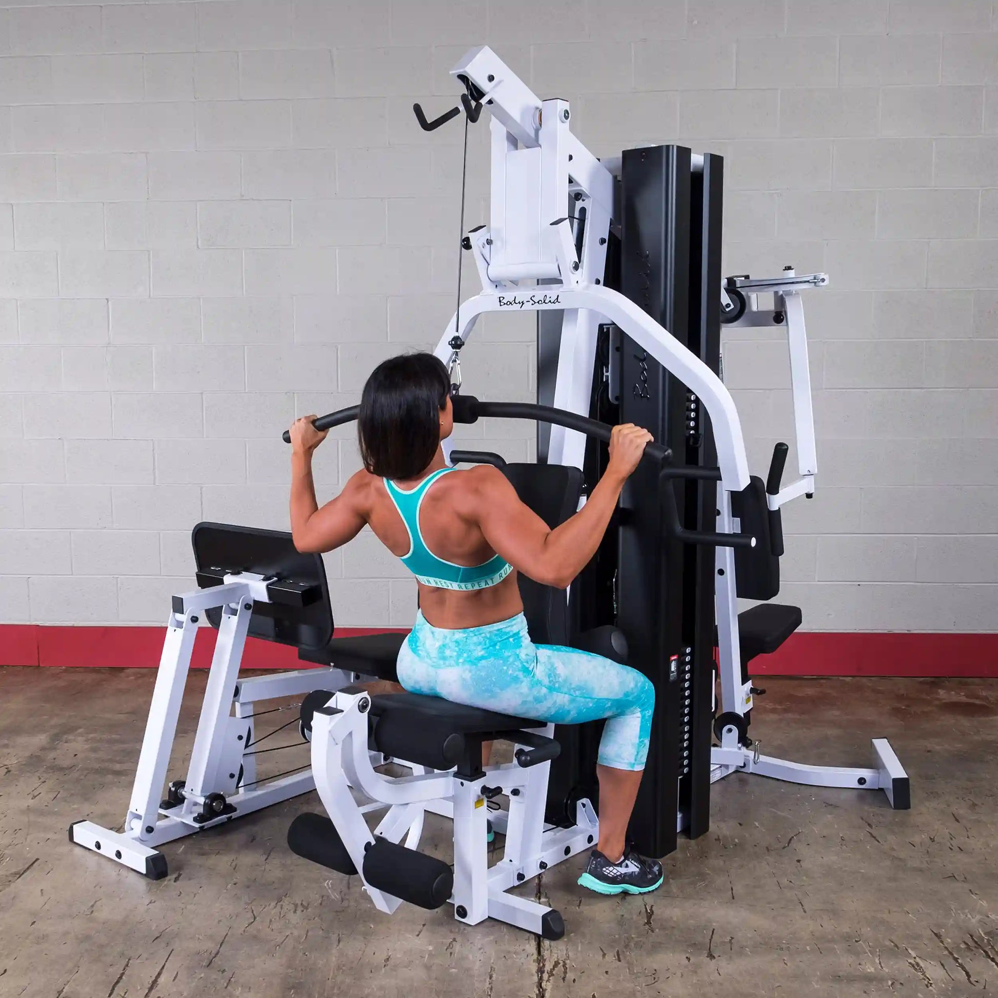 Woman using Body-Solid home gym machine in blue workout gear.
