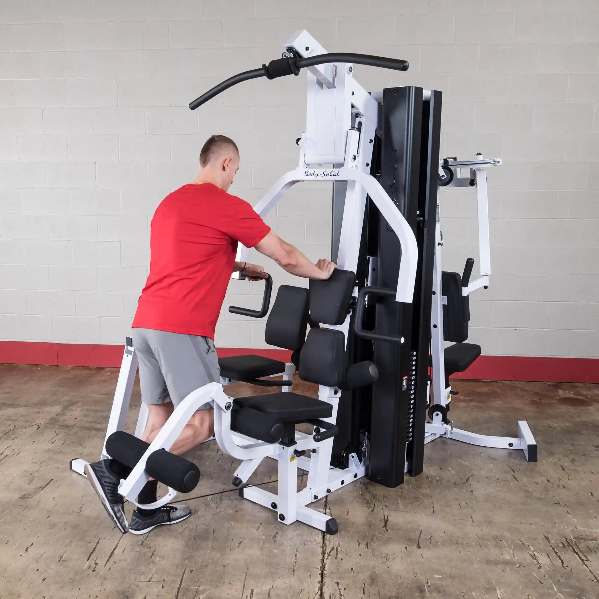 Man using Body-Solid home gym with white frame for strength training.