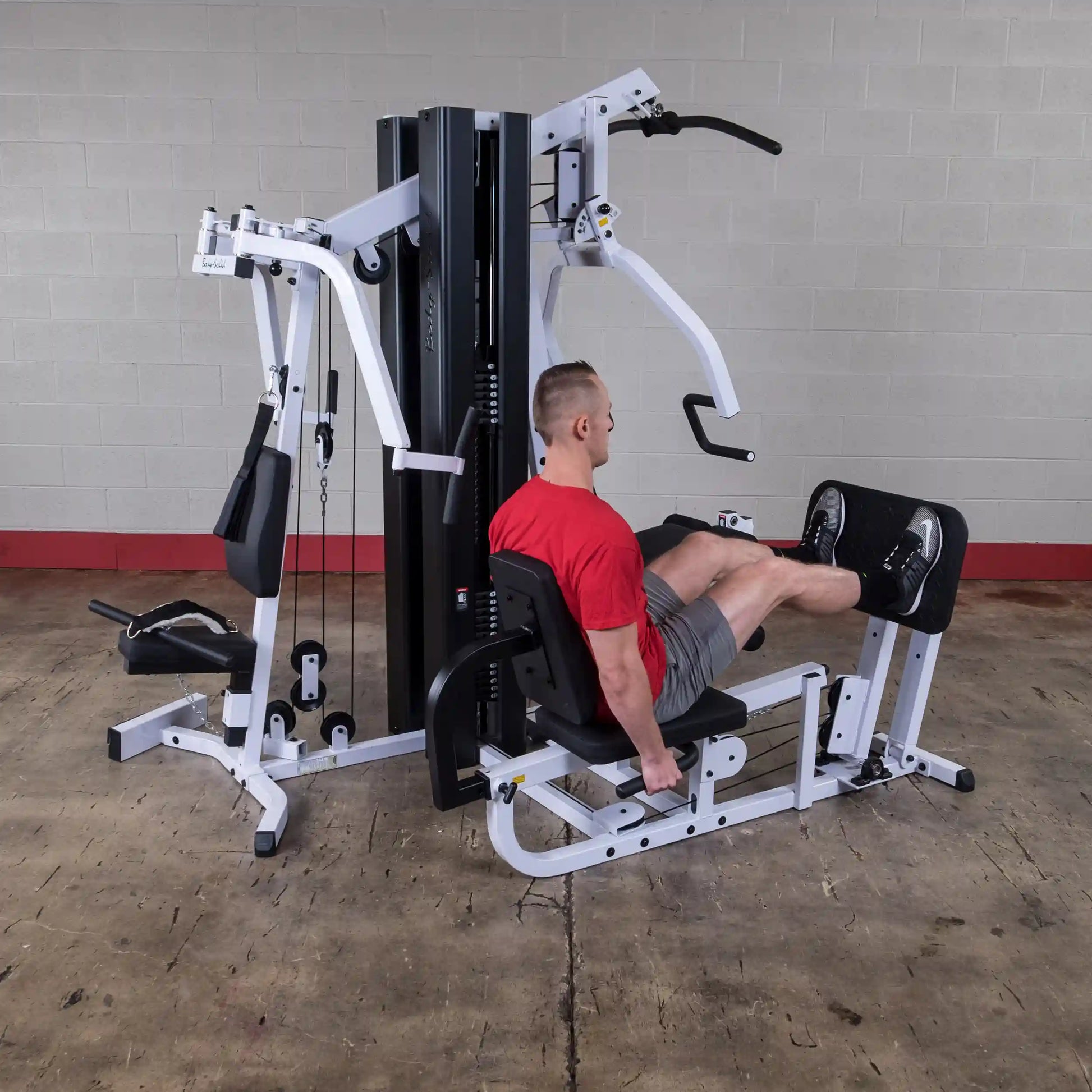 Man using Body-Solid home gym in red shirt for leg press exercise.