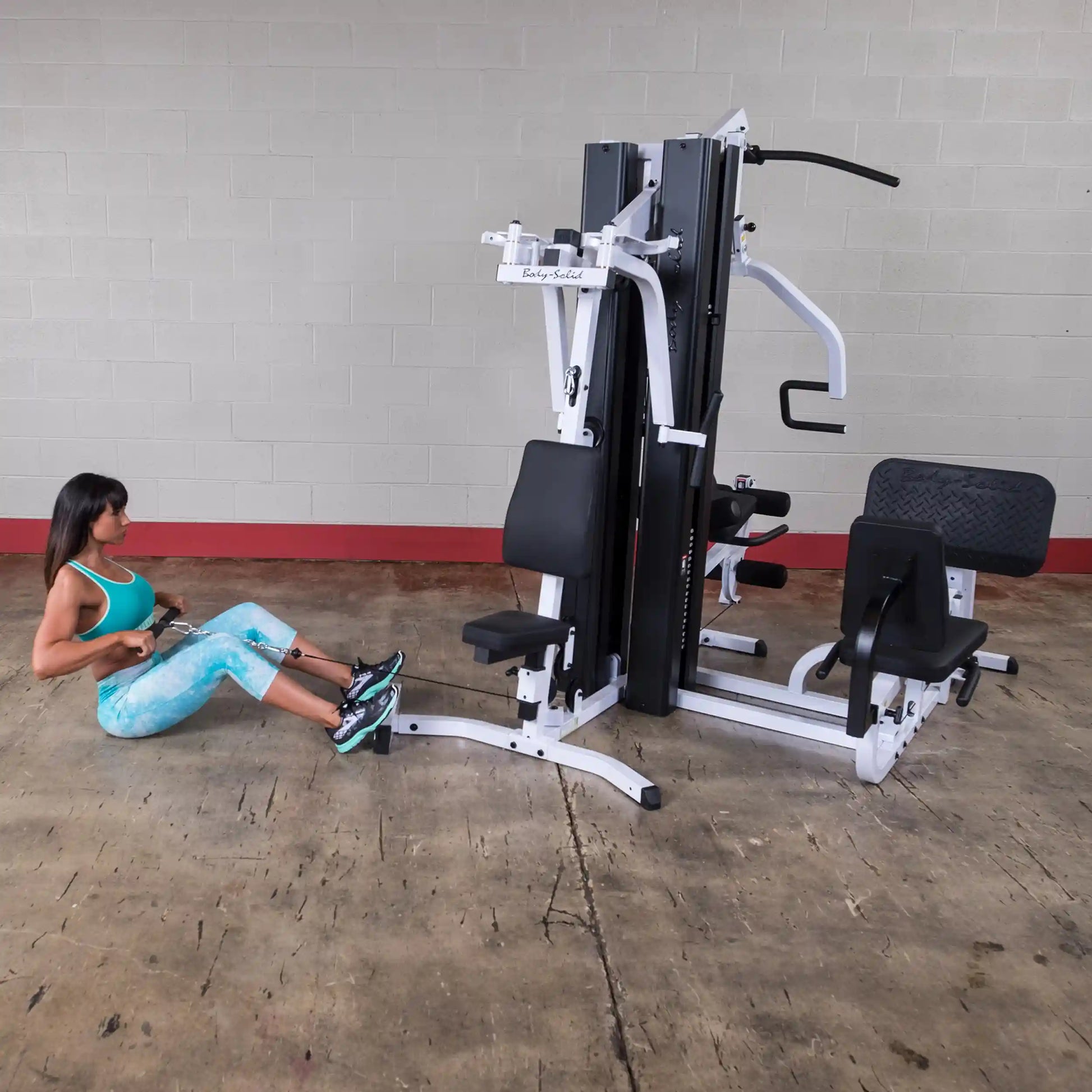 Woman using Body-Solid gym machine in turquoise activewear, performing seated row exercise.